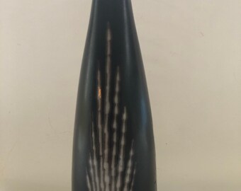 May include: A tall, black ceramic vase with a flared base and a slender, elongated neck. The vase features a white, stylized feather or plant-like design that extends upwards from the base. The vase has a smooth, glossy finish.