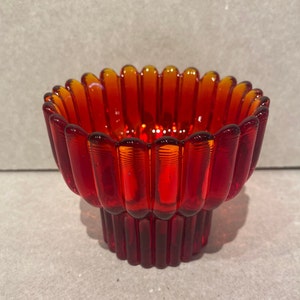 May include: A red and orange glass candle holder with a fluted design. The holder has a wide, shallow bowl and a narrow base.