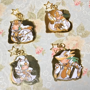 May include: Four gold-colored keychains featuring cartoon characters with white and gold accents. Each keychain has a star-shaped charm attached to a ring.