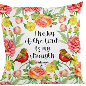 May include: White cushion with a floral pattern featuring pink, yellow, and green flowers. The cushion has a quote in black text that reads "The joy of the Lord is my strength. Nehemiah 8:10".
