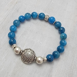 May include: A blue gemstone bracelet with silver beads and a silver charm featuring a floral design.