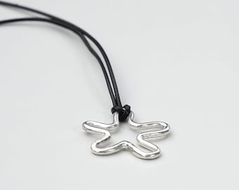 May include: A silver-colored pendant necklace featuring a five-petal flower design. The pendant is suspended from a black cord. The necklace is displayed against a white background.