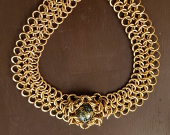 May include: A gold chainmail necklace with a large, round, green and black stone pendant.