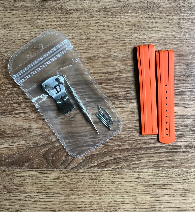 Puede incluir: Dos correas de reloj naranjas con una herramienta de correa de reloj plateada y pasadores de resorte en una bolsa de pl&aacute;stico transparente.