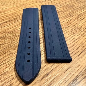 Puede incluir: Dos correas de reloj de color azul oscuro hechas de caucho con una superficie texturizada. Las correas tienen varios agujeros para ajustar el tama&ntilde;o.