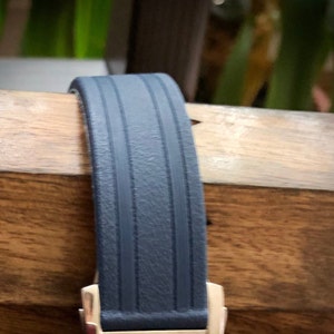 Puede incluir: Una correa de reloj azul oscuro con una superficie texturizada y dos l&iacute;neas paralelas que recorren el centro.