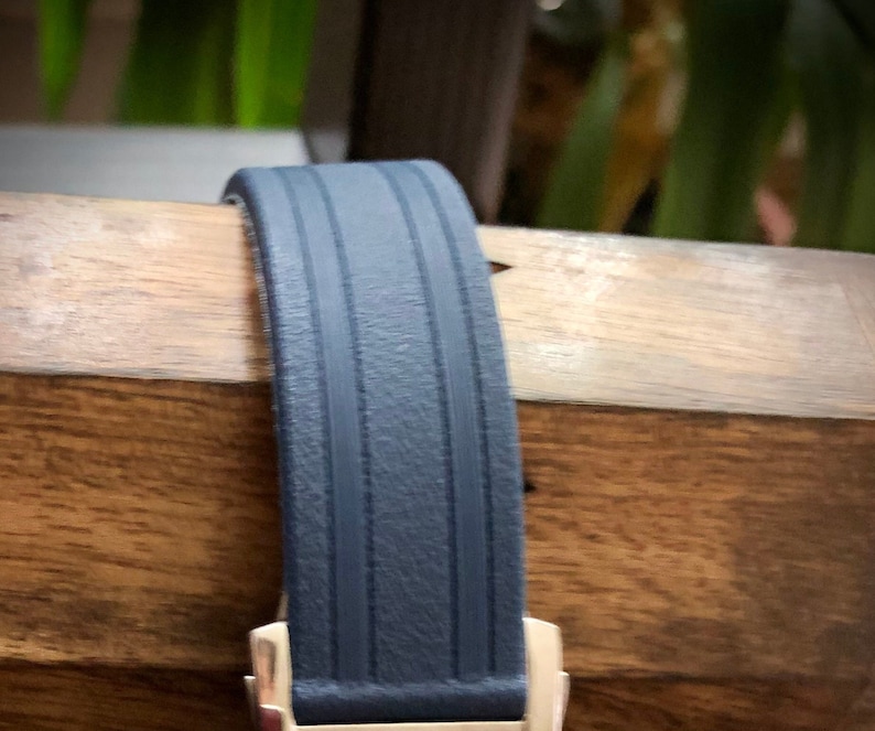 Puede incluir: Una correa de reloj azul oscuro con una superficie texturizada y dos l&iacute;neas paralelas que recorren el centro.