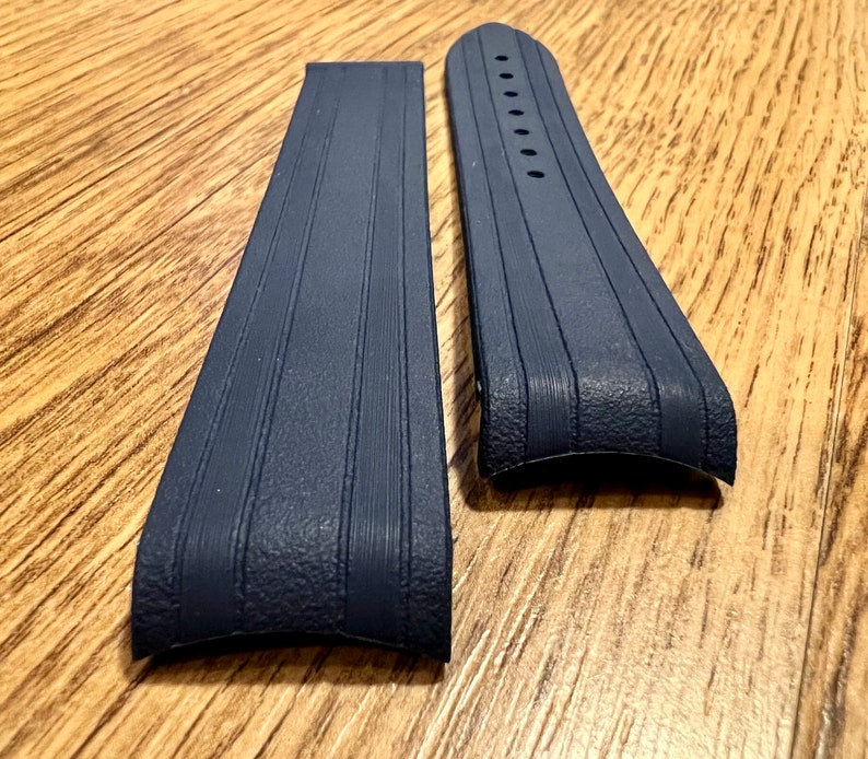 Puede incluir: Dos correas de reloj de goma azul oscuro con una superficie texturizada y una forma curva.