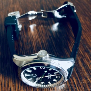 Puede incluir: Un reloj de pulsera plateado con una esfera negra y una correa de caucho negra. La esfera del reloj tiene marcas blancas y las palabras "Super Marine 100m" impresas en ella.