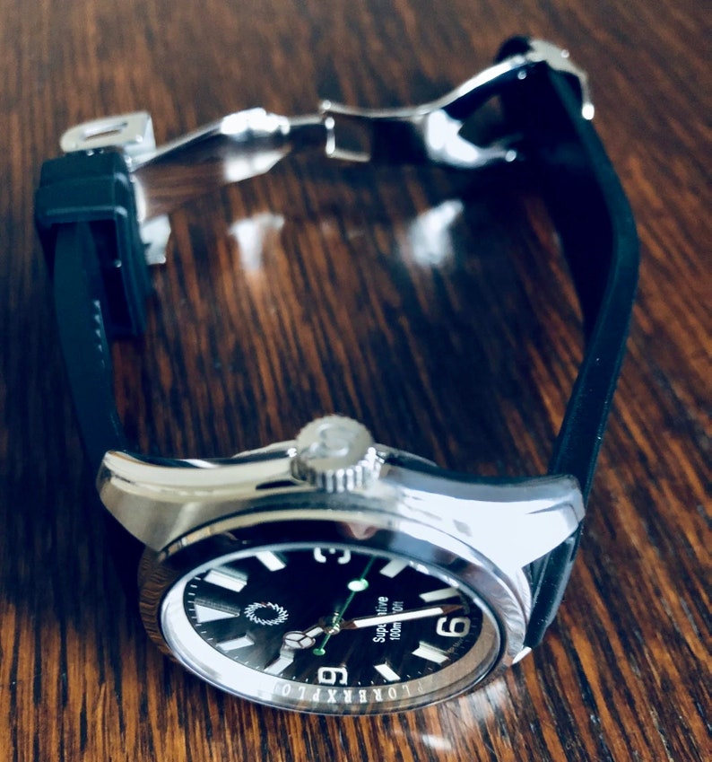 Puede incluir: Un reloj de pulsera plateado con una esfera negra y una correa de caucho negra. La esfera del reloj tiene marcas blancas y las palabras "Super Marine 100m" impresas en ella.