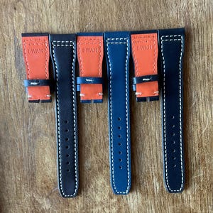 May include: Six watch straps in black and blue, with orange inner linings. Each strap has white stitching and the text "DWAH" on the orange section. The straps are displayed on a wooden surface.