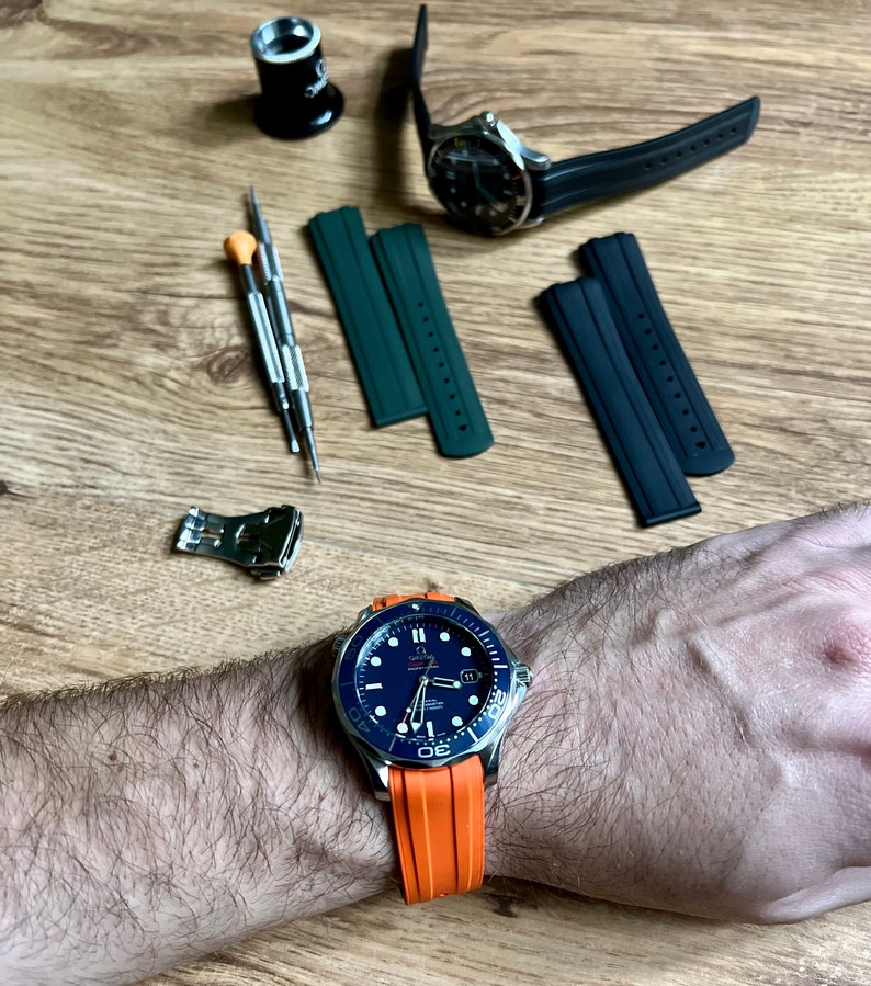 Puede incluir: Un reloj azul y plateado con una correa de caucho naranja. El reloj tiene una esfera negra con marcas blancas y una ventana de fecha en la posici&oacute;n de las 3 en punto. El reloj est&aacute; en la mu&ntilde;eca de una persona.