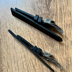 Puede incluir: Dos correas de reloj negras con hebillas plateadas. Las correas est&aacute;n hechas de un material similar al caucho y tienen una superficie texturizada.