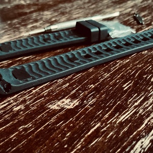 May include: Two black watch bands with a textured surface. The bands are laid out on a wooden surface.
