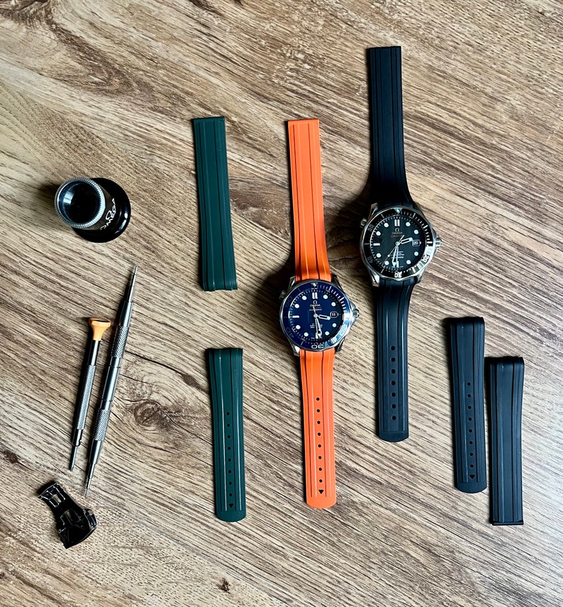 Puede incluir: Dos relojes de pulsera con esferas negras y agujas plateadas en correas de caucho de diferentes colores. Las correas son naranja y verde. Tambi&eacute;n hay cuatro correas de reloj adicionales en negro y verde.