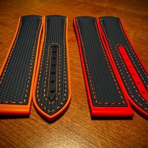 Puede incluir: Dos pares de correas de reloj. Uno es negro con detalles y costuras naranjas, el otro es negro con detalles y costuras rojas. Las correas tienen una superficie texturizada y un dise&ntilde;o curvo, adecuado para un reloj de pulsera.