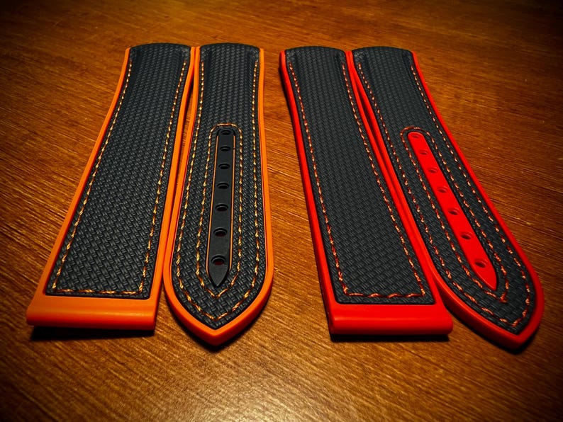 Puede incluir: Dos pares de correas de reloj. Uno es negro con detalles y costuras naranjas, el otro es negro con detalles y costuras rojas. Las correas tienen una superficie texturizada y un dise&ntilde;o curvo, adecuado para un reloj de pulsera.
