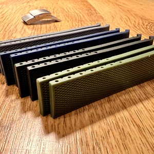 Puede incluir: Un conjunto de ocho correas de reloj en varios colores, incluyendo gris, azul, negro y verde. Las correas est&aacute;n hechas de un material texturizado y tienen un patr&oacute;n de panal. Las correas est&aacute;n dispuestas en una pila, con la correa verde en la parte superior.