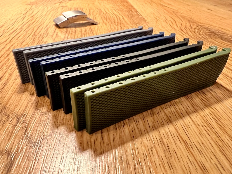 Puede incluir: Un conjunto de ocho correas de reloj en varios colores, incluyendo gris, azul, negro y verde. Las correas est&aacute;n hechas de un material texturizado y tienen un patr&oacute;n de panal. Las correas est&aacute;n dispuestas en una pila, con la correa verde en la parte superior.