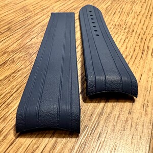 Puede incluir: Dos correas de reloj de goma azul oscuro con una superficie texturizada y una forma curva.