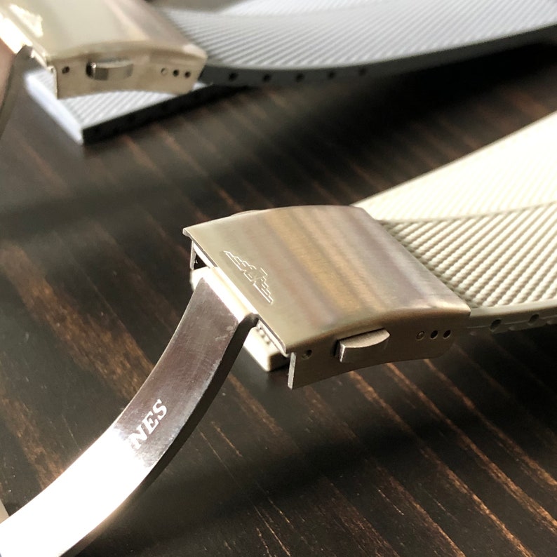 Puede incluir: Una correa de reloj plateada con una hebilla que dice "Agnes". La correa est&aacute; hecha de un material texturizado y tiene un cierre plateado.