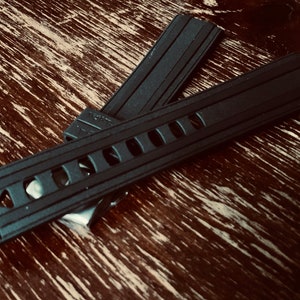 May include: Two black watch bands with a textured surface and a row of holes. The bands are made of rubber.