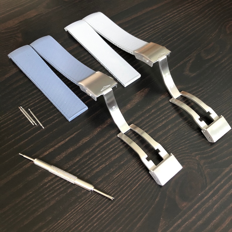 Puede incluir: Dos correas de reloj, una azul claro y otra blanca, con cierres met&aacute;licos plateados y pasadores de resorte. Las correas son de silicona y tienen una superficie texturizada.