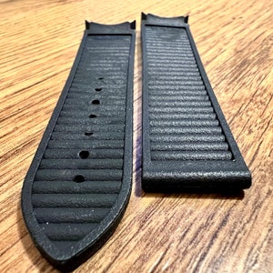 Puede incluir: Dos correas de reloj negras con textura acanalada. Las correas son de un material similar al caucho.