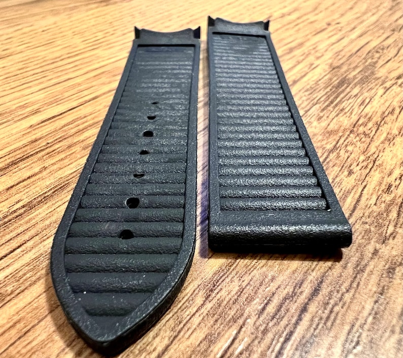 Puede incluir: Dos correas de reloj negras con textura acanalada. Las correas son de un material similar al caucho.