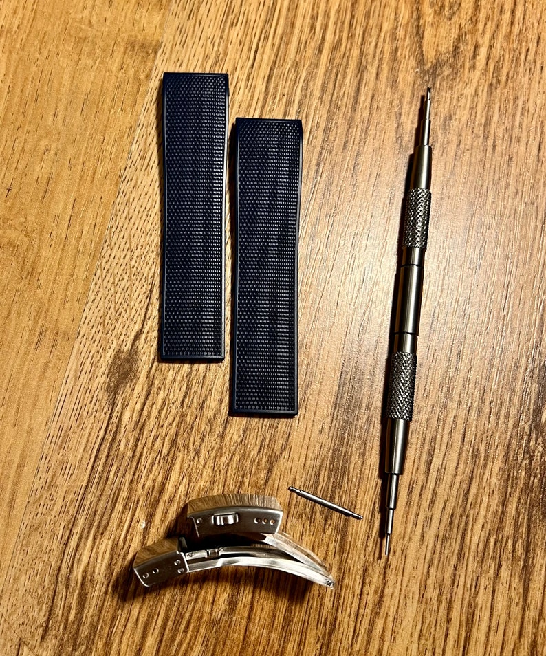 Puede incluir: Dos correas de reloj negras con una superficie texturizada y una correa de reloj plateada con una herramienta de pasador de resorte.