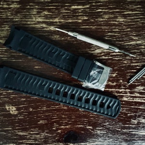 May include: Two black watch bands with a silver tool for adjusting the bands.