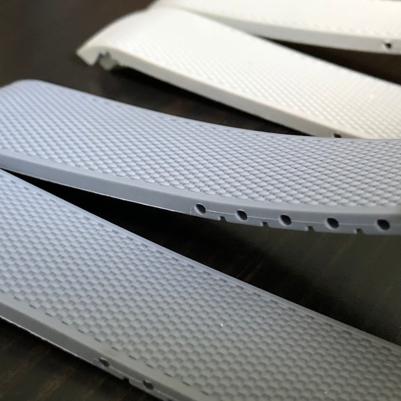 Puede incluir: Dos correas de reloj grises con una superficie texturizada y peque&ntilde;os agujeros a lo largo del borde.