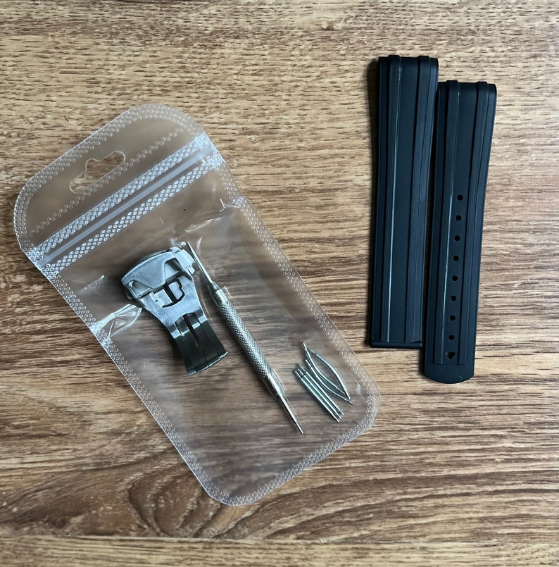 Puede incluir: Un juego de correas de reloj negras con una herramienta de barra de resorte plateada y barras de resorte en una bolsa de pl&aacute;stico transparente.