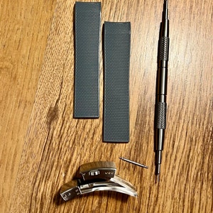 Puede incluir: Dos correas de reloj grises con una superficie texturizada, una correa de reloj plateada y una herramienta plateada para quitar las correas de reloj.