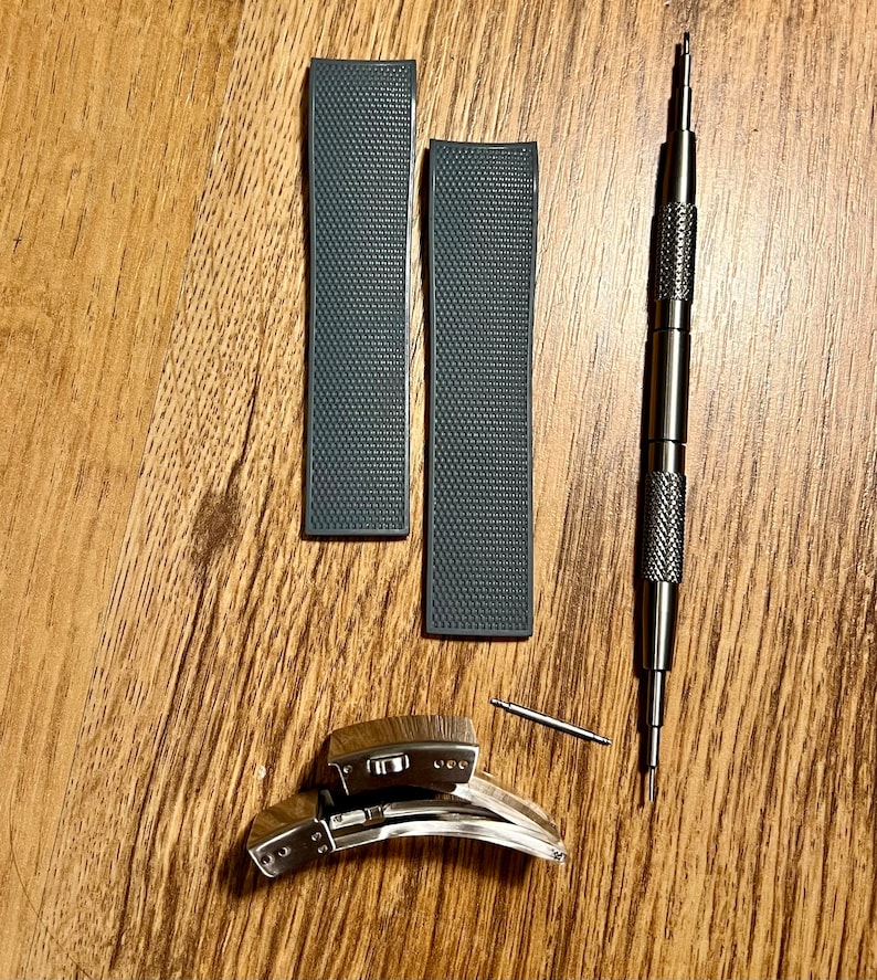 Puede incluir: Dos correas de reloj grises con una superficie texturizada, una correa de reloj plateada y una herramienta plateada para quitar las correas de reloj.