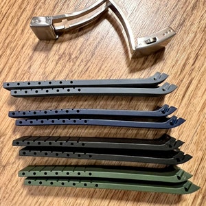 Puede incluir: Cuatro correas de reloj en diferentes colores: negro, azul oscuro, verde y gris. Las correas son de goma y tienen una superficie texturizada. Tambi&eacute;n se muestra una hebilla de reloj plateada.