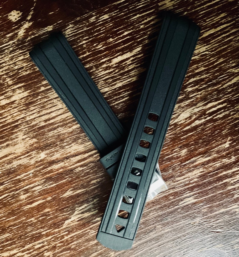 May include: Two black watch straps with a textured surface and a row of holes. The strap on the left has the word "Veston" printed on it.