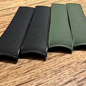 Puede incluir: Cuatro correas de reloj, dos negras y dos verdes, con una superficie texturizada.