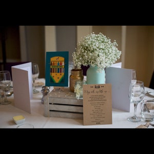 May include: A wedding table centerpiece with a rustic wooden crate, a teal mason jar filled with white baby's breath, and a sign that reads "I Do with my little one..."