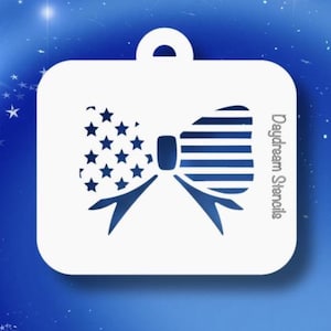 May include: White stencil featuring a bow design with stars and stripes, reminiscent of the American flag. The stencil has a rounded rectangular shape with a loop at the top. The text "Daydream Stencils" is printed on the side.