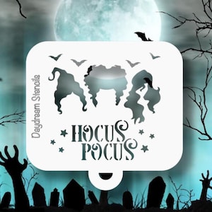 May include: A white stencil with the words "Hocus Pocus" and silhouettes of three witches. The stencil also features stars and bats, with the words "Daydream Stencils" on the side. The background is a spooky scene with a full moon.