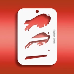 May include: A white stencil featuring two red buffalo head logos, with a small hole at the top for hanging. The stencil has rounded corners and the text "Daydream Stencils" is printed on the side. The background is a gradient of red.