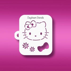 May include: A white rectangular stencil with rounded corners featuring the text Daydream Stencils at the top. The design includes a cat face with a bow, two small flowers, and a separate bow shape cut out from the material for crafting projects.