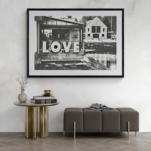 May include: Black and white photograph of a building with the word "LOVE" in large letters on the side. The building is located on a waterfront with a small boat dock in the foreground.