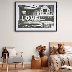 May include: Black and white photograph of a building with the word "LOVE" in large letters on the side. The photo is framed in a black frame and hanging on a white wall.