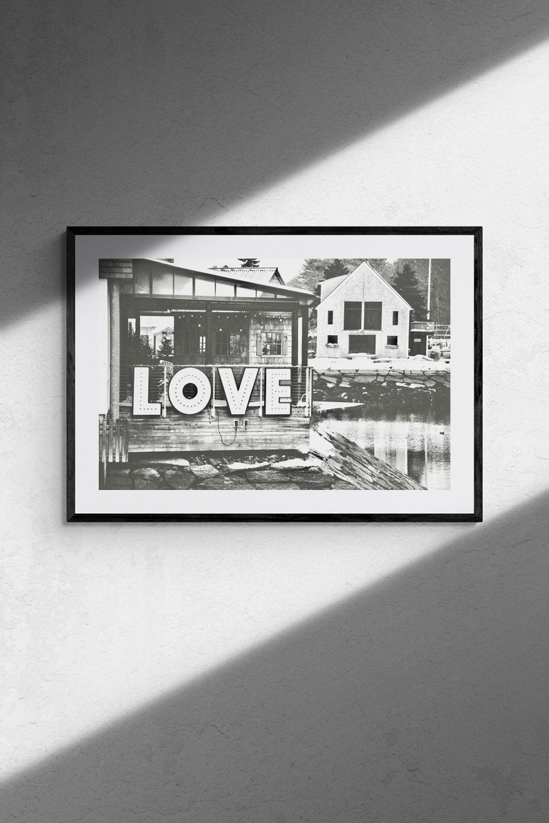 May include: Black and white photograph of a building with a sign that says "LOVE" in large, bold letters. The building is located on a waterfront with a small body of water in the foreground.