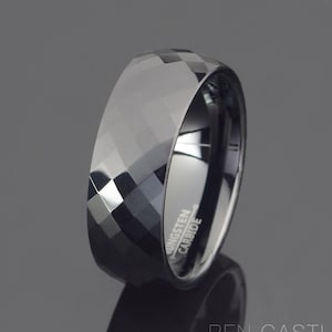 May include: A black tungsten carbide ring with a faceted design. The ring is engraved with "Tungsten Carbide".