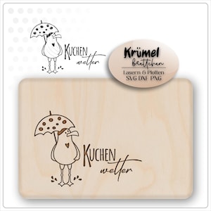May include: A rectangular wooden cutting board with a whimsical design. It features a cartoon bird under a polka-dot umbrella, with the words "Kuchen Wetter" in a handwritten font. An oval label reads "Krümel Brettchen".