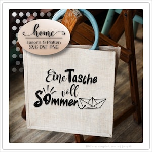 Pu&ograve; includere: Una borsa tote beige con manici azzurri. La borsa presenta un testo nero che recita "Eine Tasche voll Sommer" e un'illustrazione di barchetta di carta. Un adesivo ovale con la parola "home" &egrave; attaccato alla borsa.