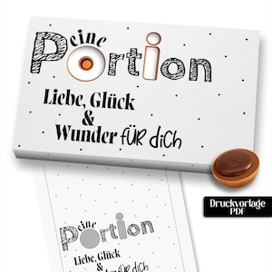 Könnte beinhalten: Eine weiße rechteckige Karte mit dem Text "Deine Portion Liebe, Glück & Wunder für dich" in Schwarz, wobei ein kreisförmiger Ausschnitt den Buchstaben "o" in "Portion" ersetzt. Ein braunes Schokoladenbonbon liegt neben der Karte, mit PDF-Symbol.
